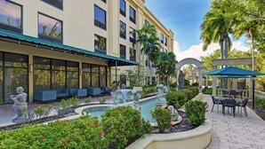 A courtyard with a fountain, seating areas, and a building with large windows. - Hampton Inn Palm Beach Gardens (Palm Beach Gardens)