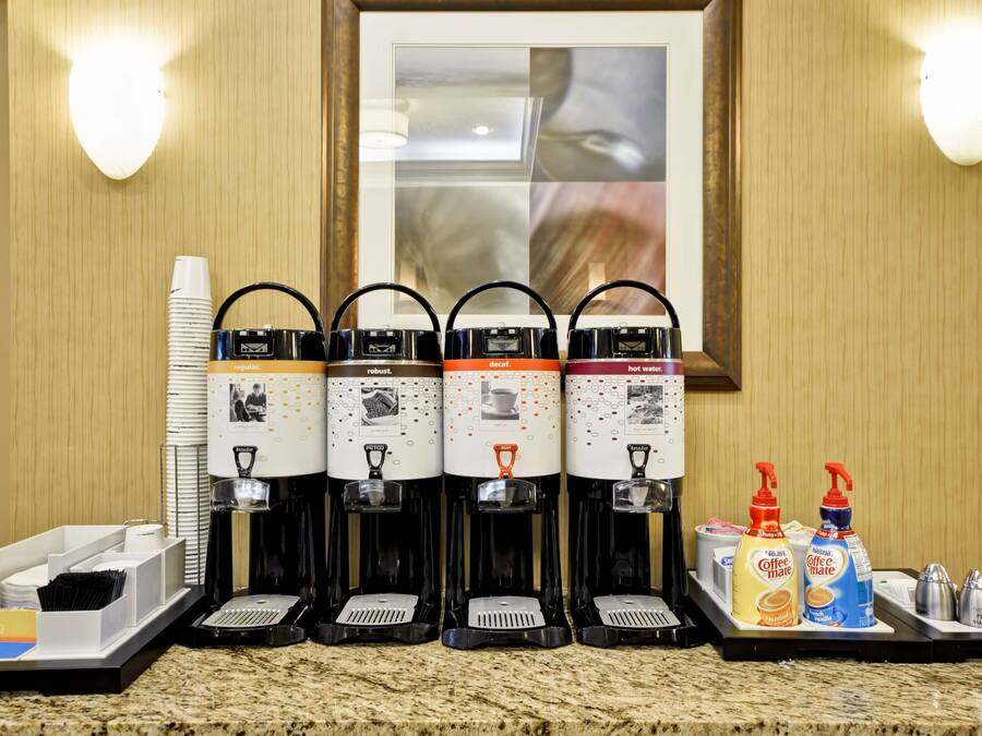 Una estación de café con cuatro máquinas de café, vasos desechables y aderezos.
