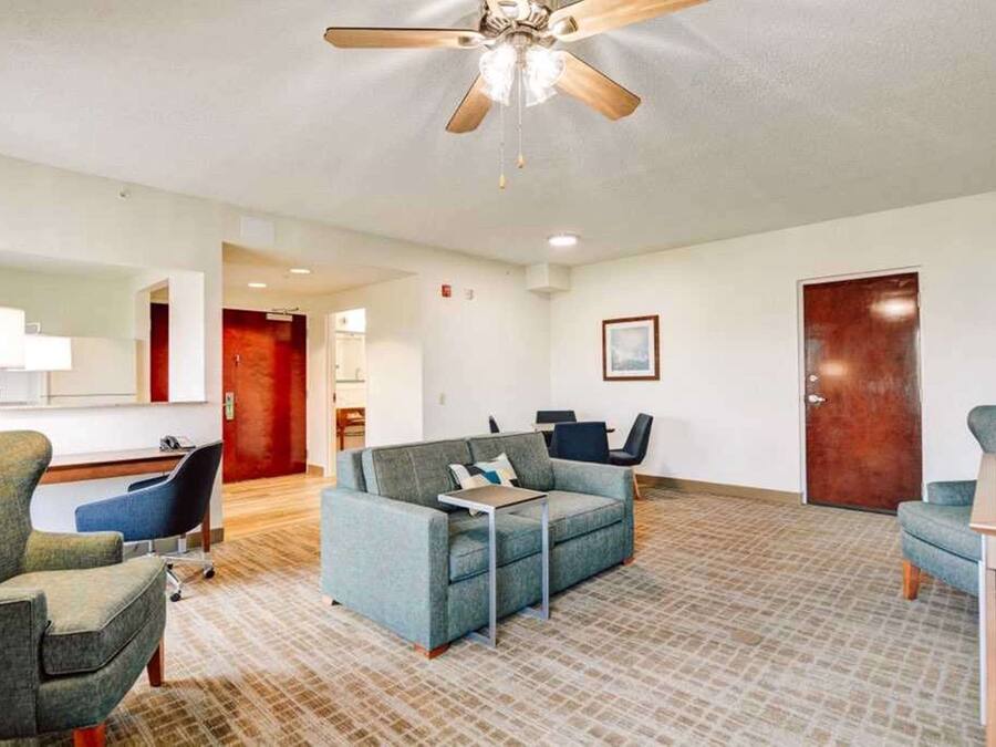 Ein Hotelzimmer mit Sofa, Stühlen, einem Schreibtisch, einem Deckenventilator und einer Tür.