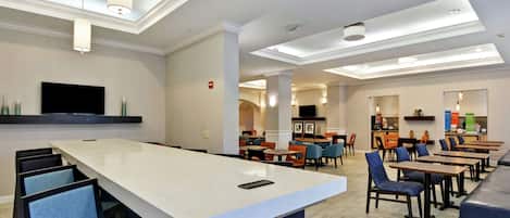 A modern hotel lobby with a central bar area, seating arrangements, and a flat-screen TV mounted on the wall.