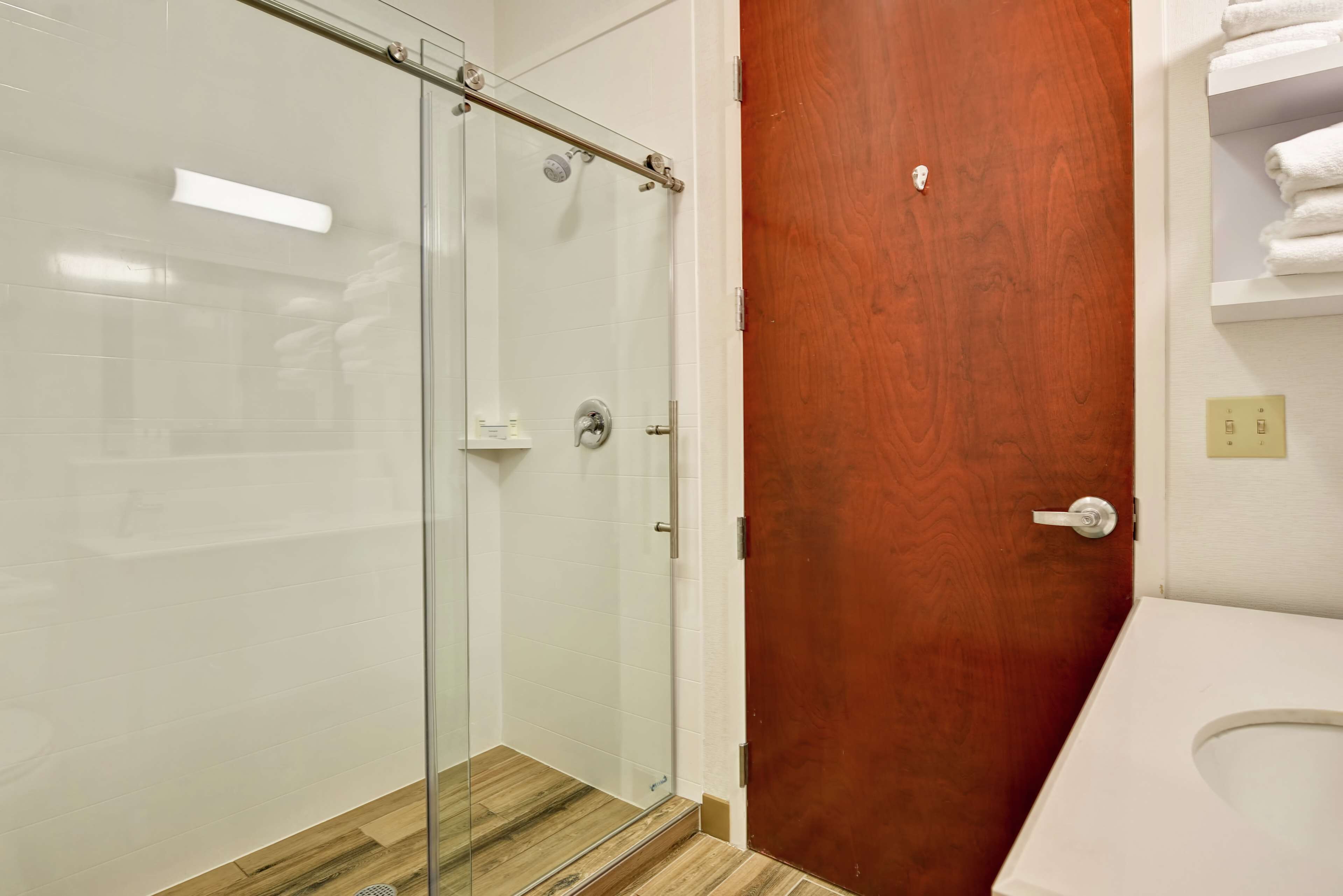 A bathroom with a glass-enclosed shower, a wooden door, and a white toilet.