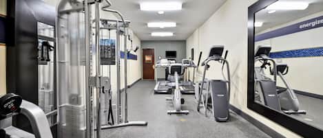 Un gimnasio con máquinas de cardio, máquinas de pesas y un espejo grande.