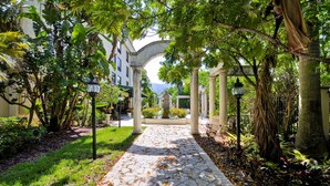 A stone-paved pathway flanked by lush greenery and columns, leading to a building with an arched entrance. - Hampton Inn Palm Beach Gardens (Palm Beach Gardens)