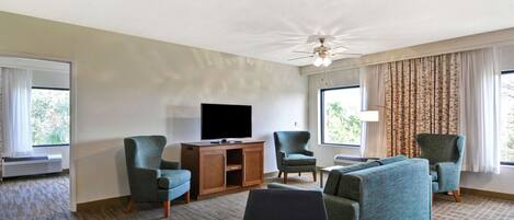 Une chambre d’hôtel équipée d’une télévision, de deux fauteuils, d’un canapé, d’une table à manger et d’un ventilateur de plafond.
