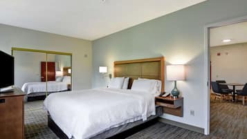 Hotelkamer met een groot bed, nachtkastjes, een bureau, een televisie, een spiegel en een zithoek met stoelen en een tafel.