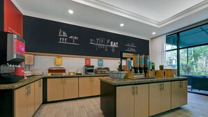 A modern kitchen with a central island, wooden cabinets, and a black backsplash with food-related graphics. - Hampton Inn Palm Beach Gardens (Palm Beach Gardens)