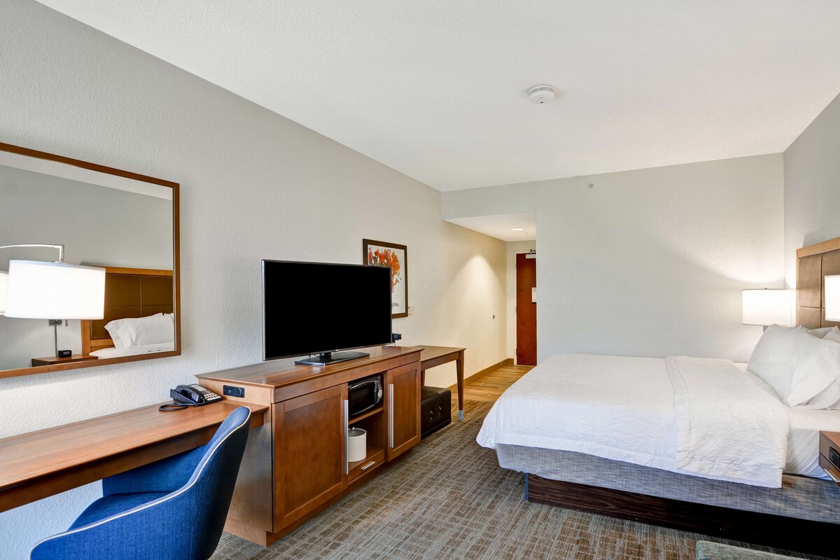 A hotel room with a bed, a desk with a computer, a television, and a mirror.