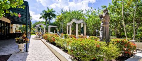 A landscaped garden with a statue, a covered seating area, and a building with a green awning.