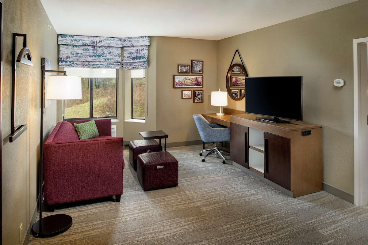 A compact hotel room with a red sofa, a small desk with a TV, a lamp, and framed pictures on the wall.