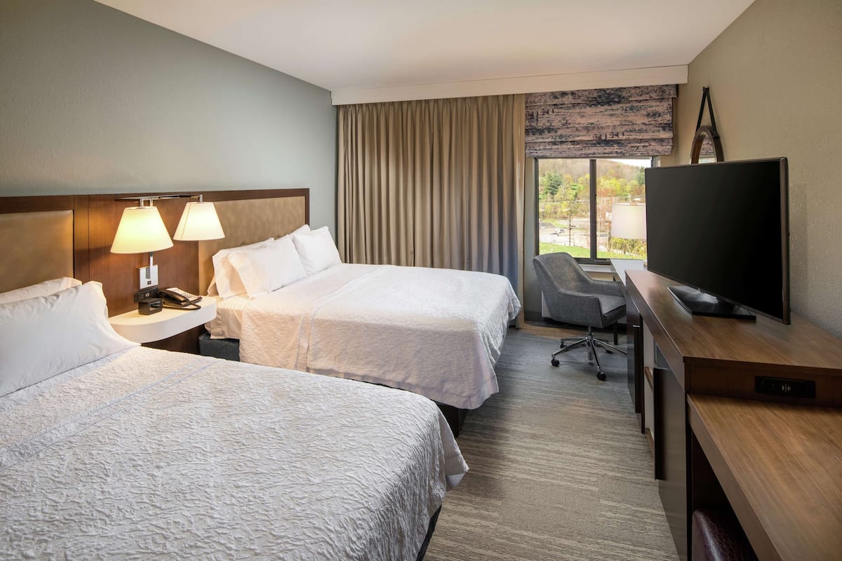 A hotel room with two beds, a desk with a television, and a window with curtains.