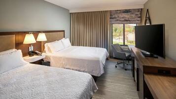 A hotel room with two beds, a desk with a television, and a window with curtains.
