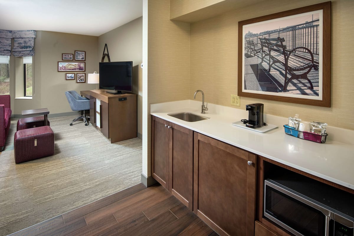 A compact hotel room with a kitchenette, a seating area with a TV, and a dining table.