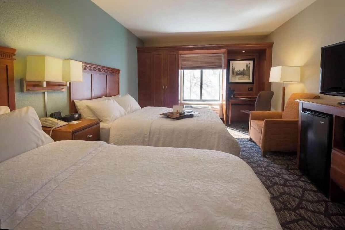 A hotel room with two beds, a desk, a chair, a television, and a window.