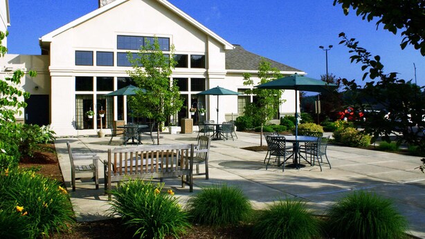A building with a patio area featuring outdoor seating and umbrellas. - Hampton Inn & Suites Binghamton/Vestal (Vestal)