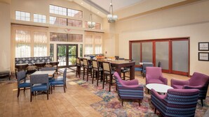 A spacious lobby with a high ceiling, multiple seating areas, and a large window providing natural light. - Hampton Inn & Suites Binghamton/Vestal (Vestal)