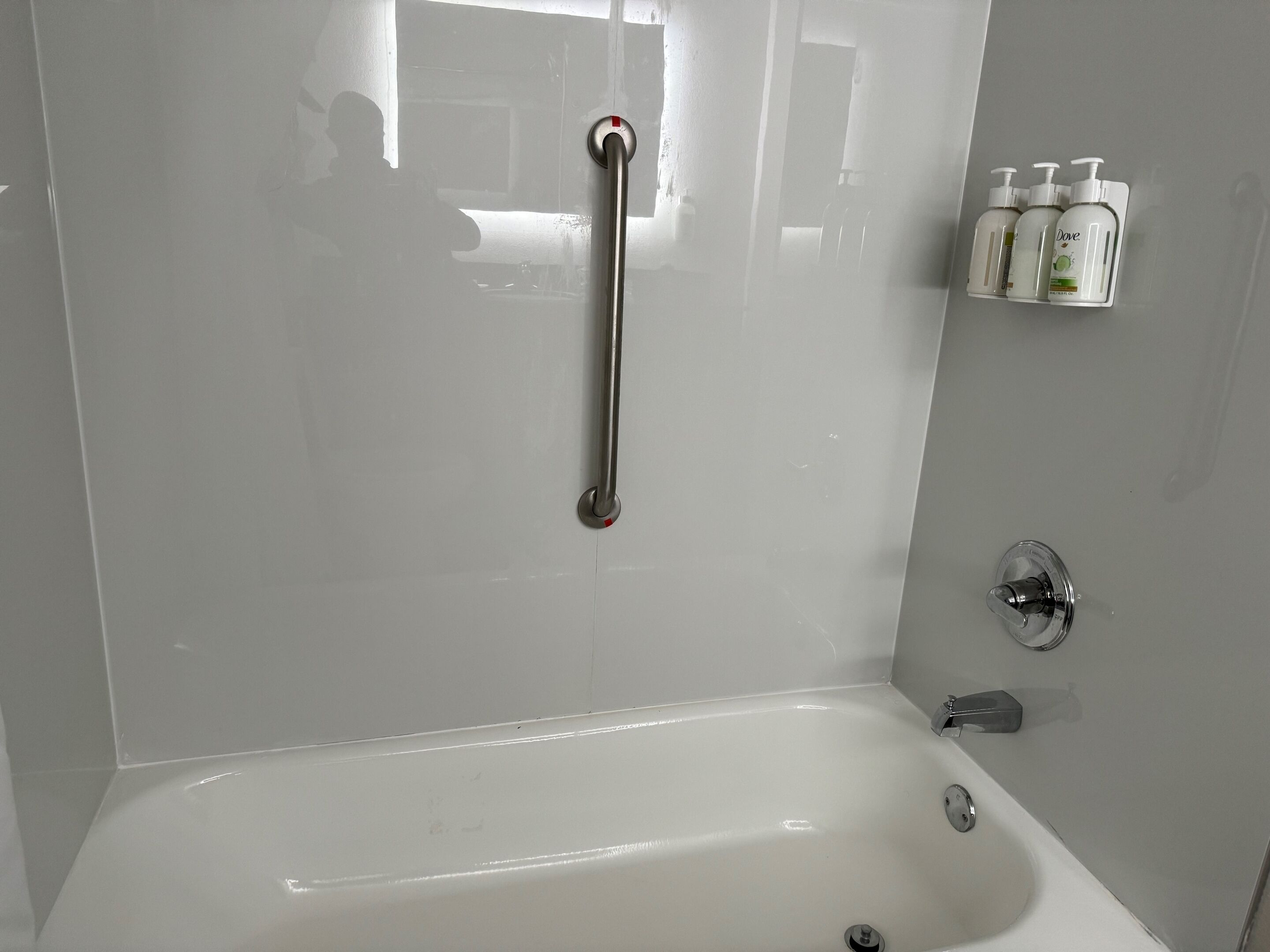 Un baño con una bañera blanca, una barra de apoyo, un cabezal de ducha y un estante con artículos de aseo.