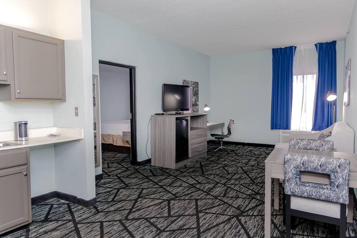 Une chambre d’hôtel équipée d’une kitchenette, d’une télévision, d’un bureau, d’une chaise et d’un lit.
