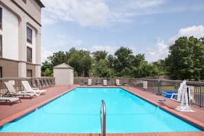 Piscina rectangular con escalera metálica, rodeada de sillas de descanso y una valla.