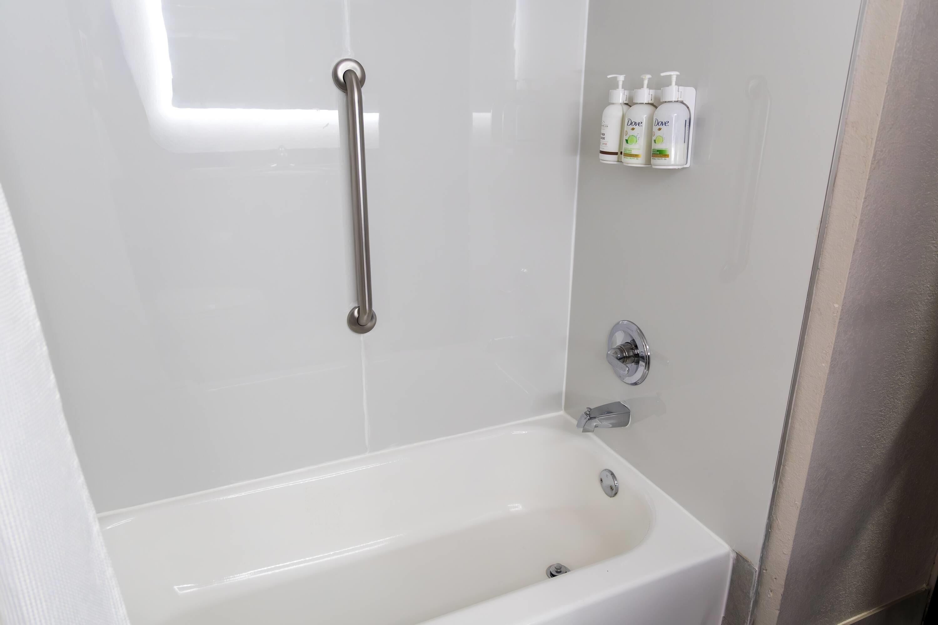 Une salle de bain avec une baignoire blanche, une barre d’appui et une étagère contenant des produits Dove.