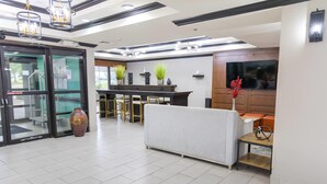 Un vestíbulo de hotel con mostrador de recepción, zona de estar y una gran pantalla de televisión.