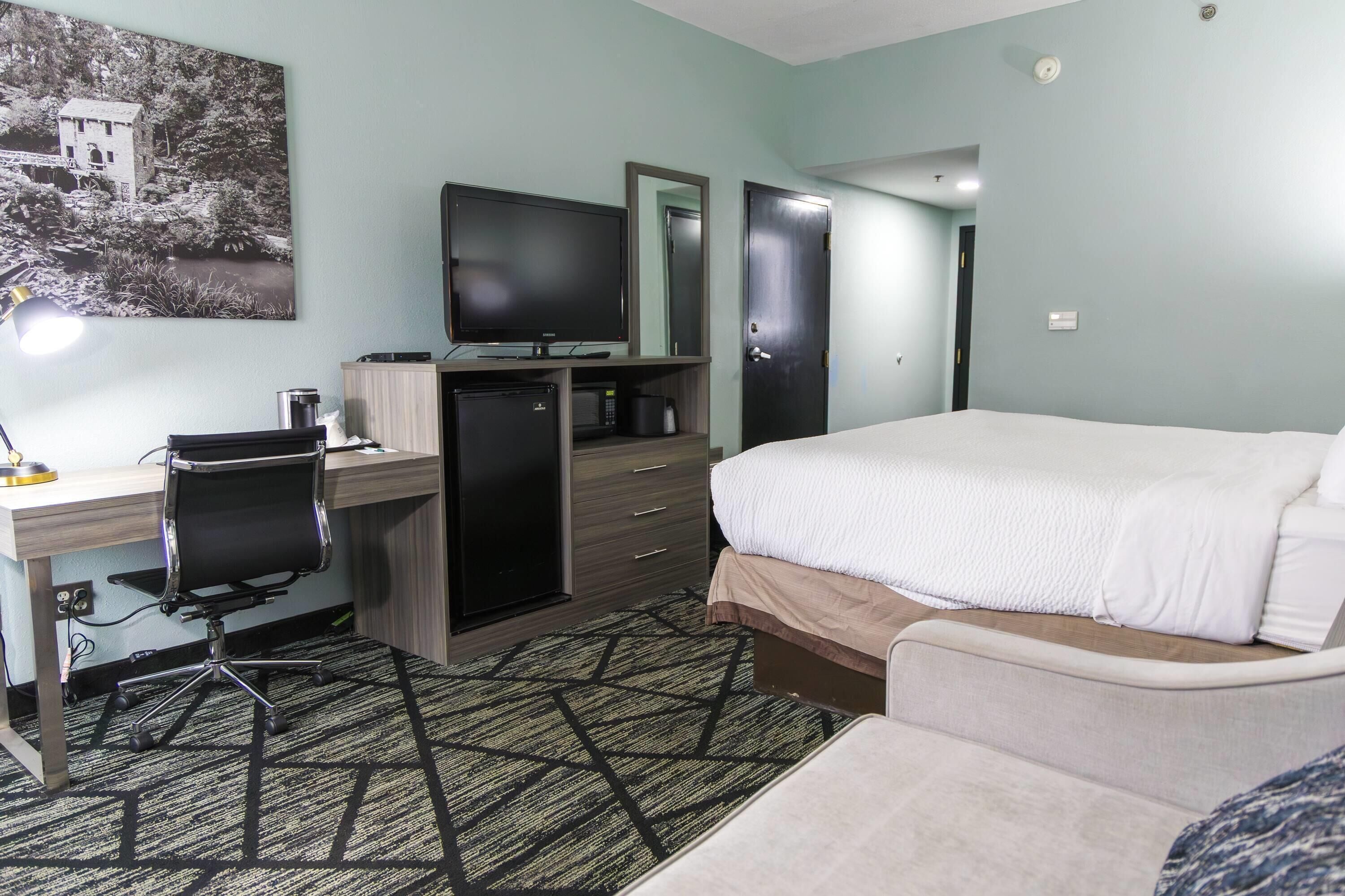 Une chambre d’hôtel équipée d’un lit, d’un bureau, d’une chaise, d’une télévision et d’un four à micro-ondes.