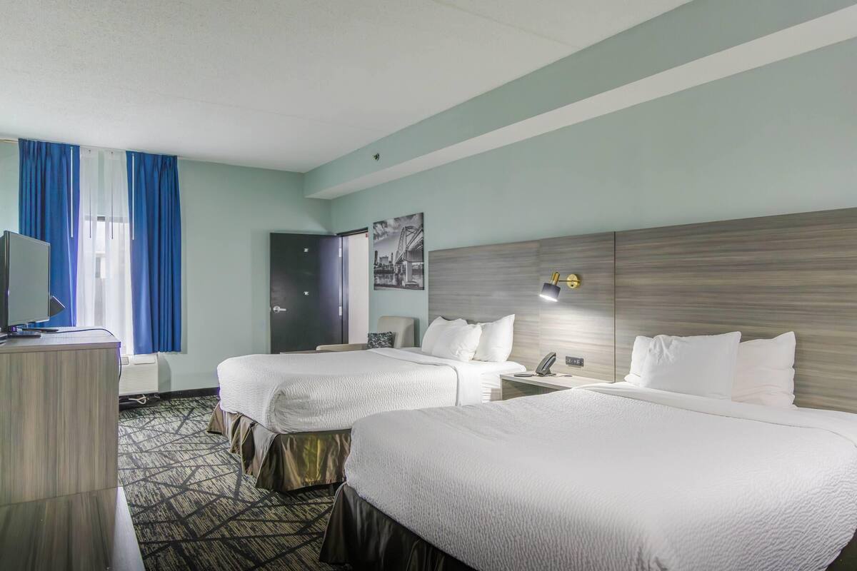 Une chambre d’hôtel avec deux lits, un bureau, une télévision et une porte.