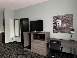 Habitación de hotel con escritorio, televisión, microondas, una silla y un cuadro en la pared.