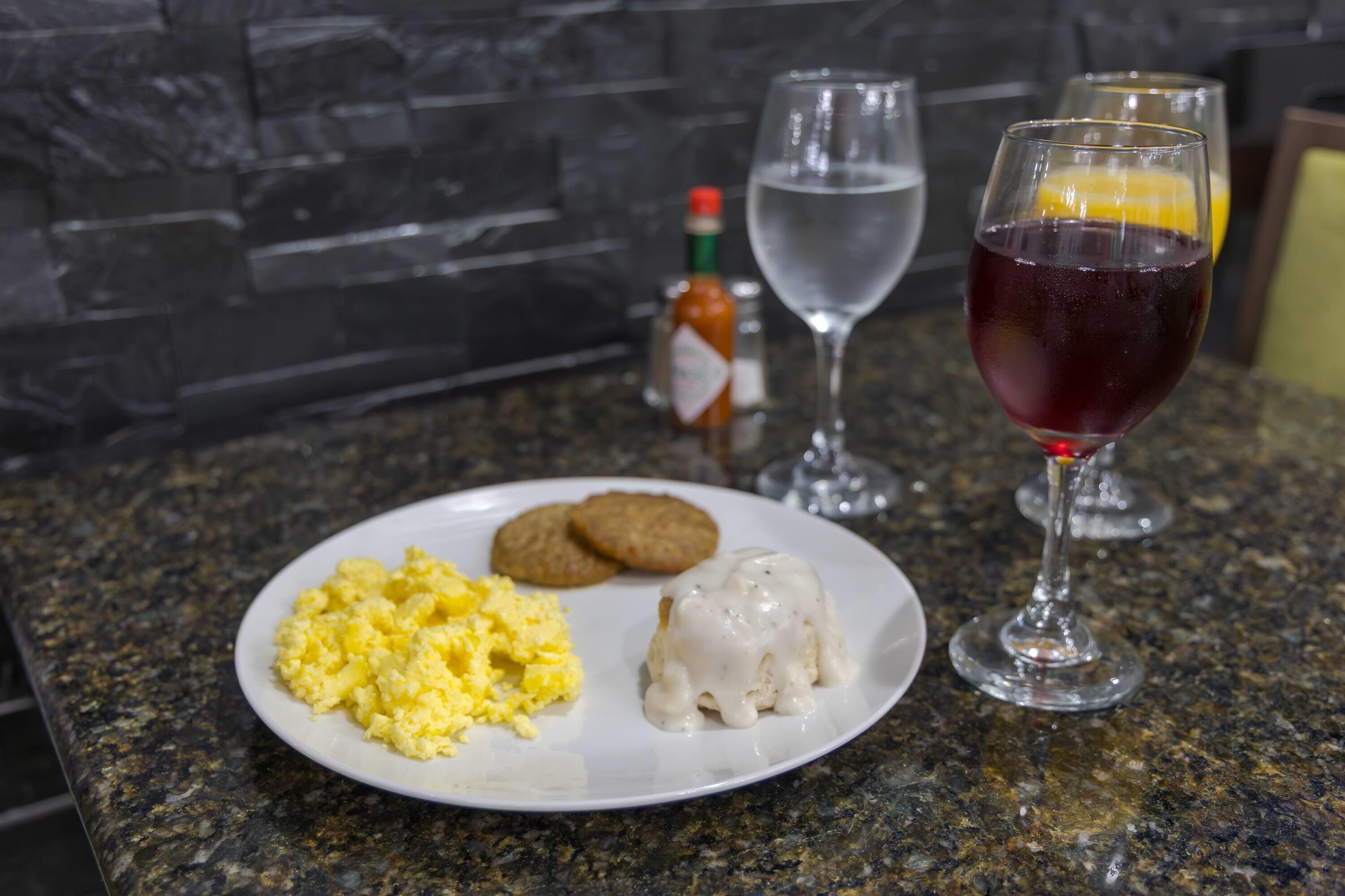 A breakfast plate with scrambled eggs, a white sauce, and cookies on a granite countertop.