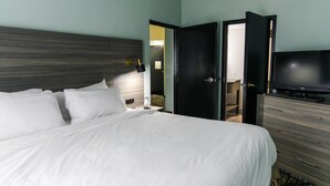 Una habitación de hotel con cama, televisor, cómoda y puerta que da a otra habitación.