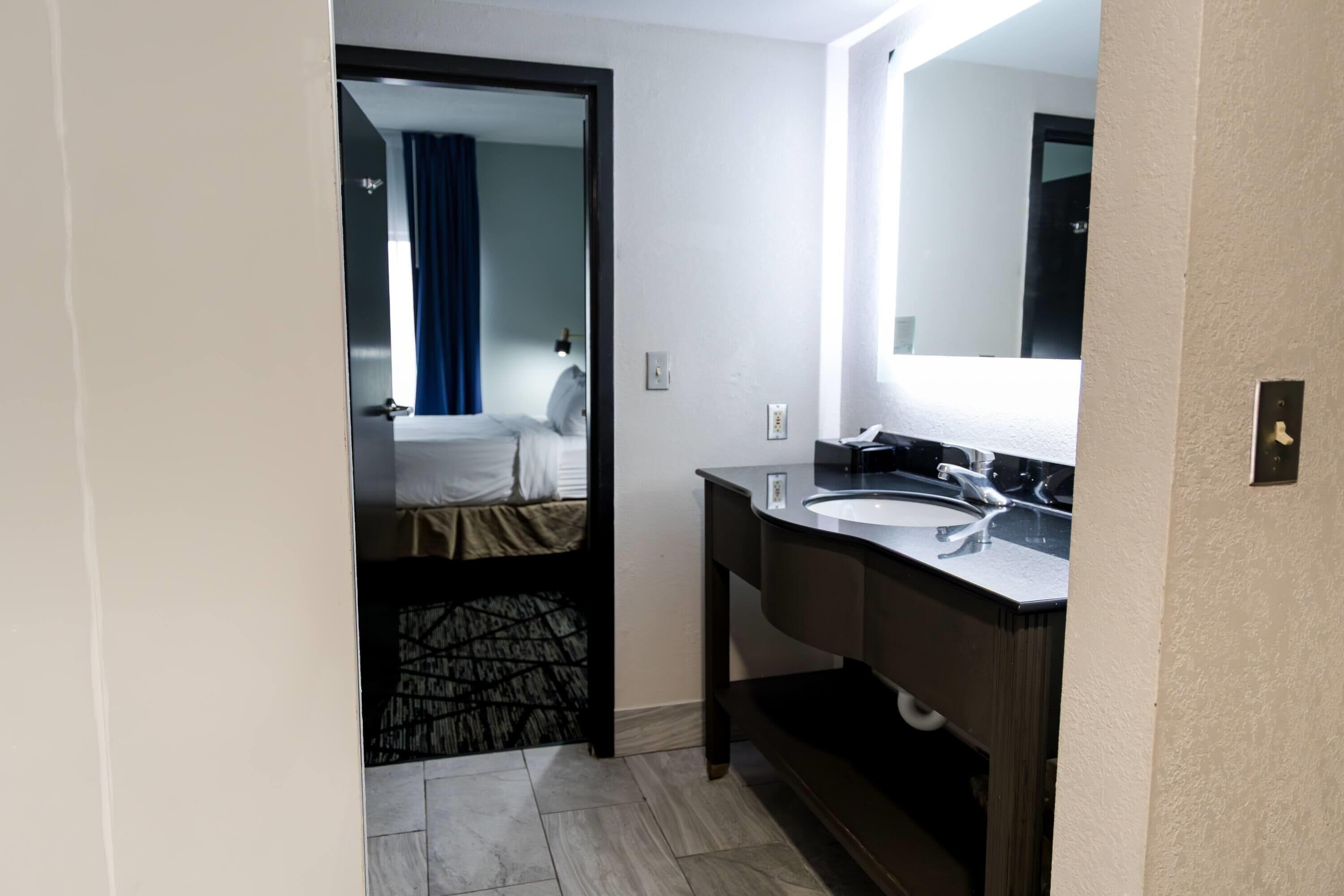 Une chambre d’hôtel comprenant un lit, une salle de bain avec un lavabo et un miroir, et une porte donnant sur une autre pièce.
