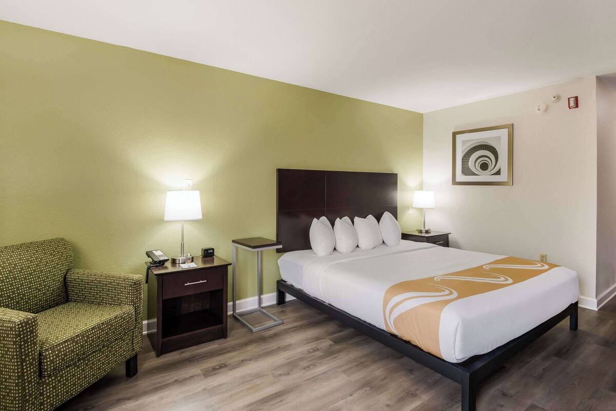 A hotel room with a bed, a chair, a nightstand, and a lamp.