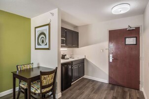 Cocina compacta con microondas, pileta y lavavajillas, junto a un comedor con mesa y sillas.