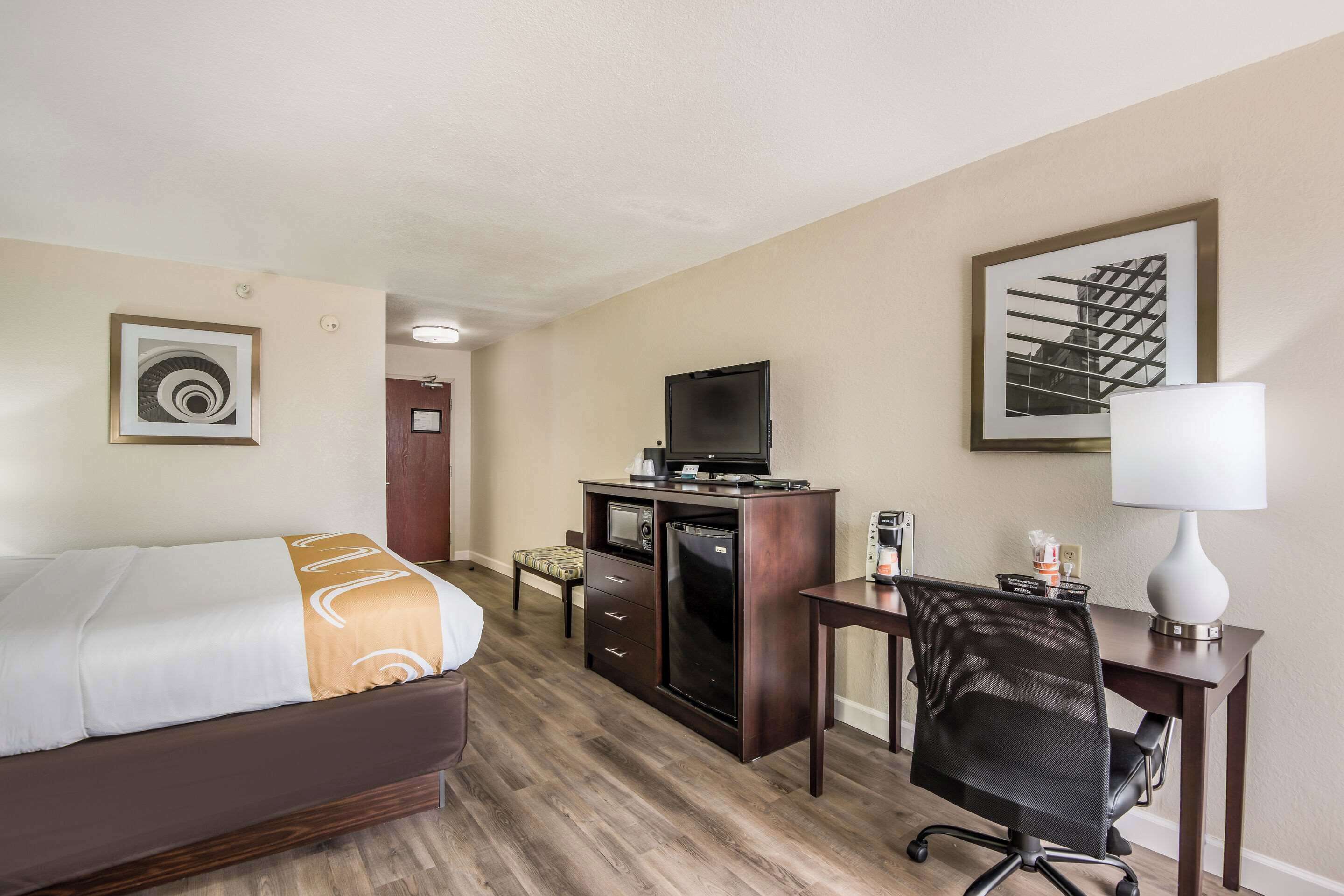 Een hotelkamer met een bed, bureau, stoel, televisie, koelkast en kunst aan de muren.