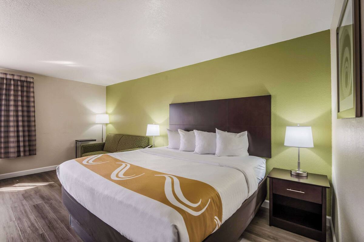 A hotel room with a large bed, two bedside tables with lamps, a green accent wall, and a plaid curtain.