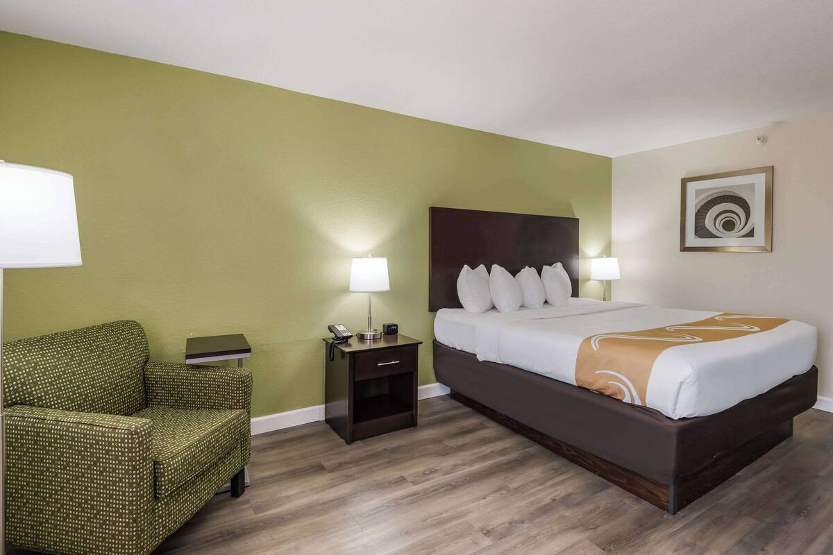 A hotel room with a bed, a nightstand, a chair, and a lamp.