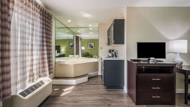A hotel room with a bed, a desk with a computer, a TV, and a bathroom with a shower. - Quality Inn & Suites Quincy - Downtown (Quincy)