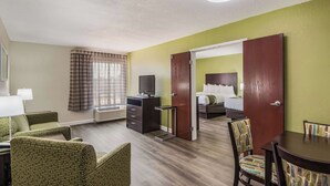 A hotel room with a bed, a desk with a chair, a television, and a dining area with chairs. - Quality Inn & Suites Quincy - Downtown (Quincy)