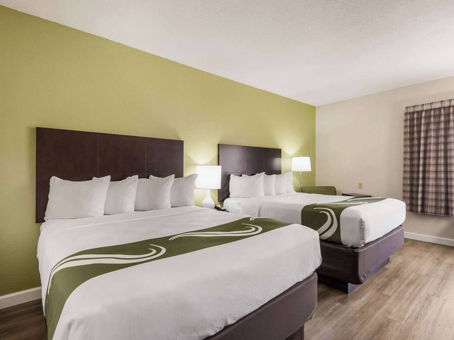 A hotel room with two beds, green walls, and a window with curtains.
