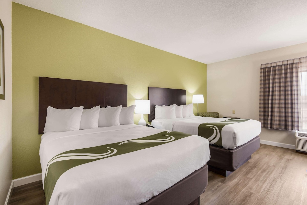 A hotel room with two beds, a green wall, and a window with curtains.