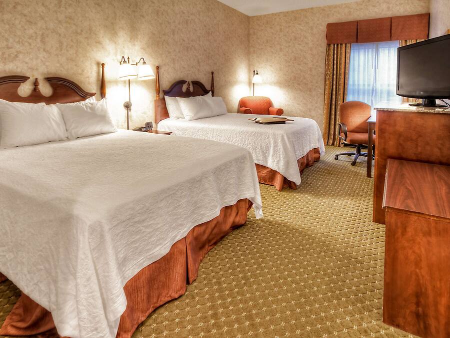 A hotel room with two beds, a desk with a television, and a chair.