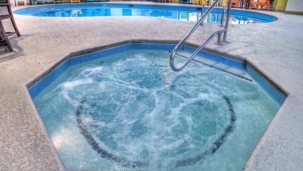 Una piscina interior con un jacuzzi, rodeada de sillas Adirondack de colores y una mesa con sillas.