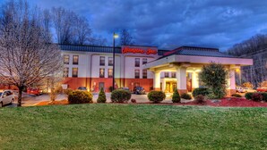 A Hampton Inn hotel with a red and white facade, a covered front entrance, and a parking lot with several cars.