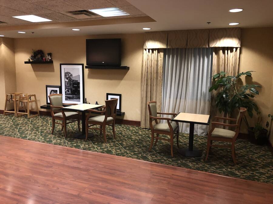A conference room with a long table, several chairs, a television on the wall, and a large window with curtains.