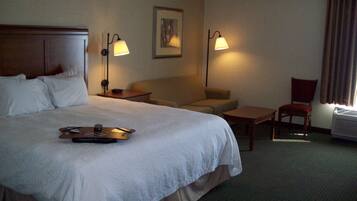 A hotel room with a large bed, a sofa, a chair, a small table, and two wall-mounted lamps.