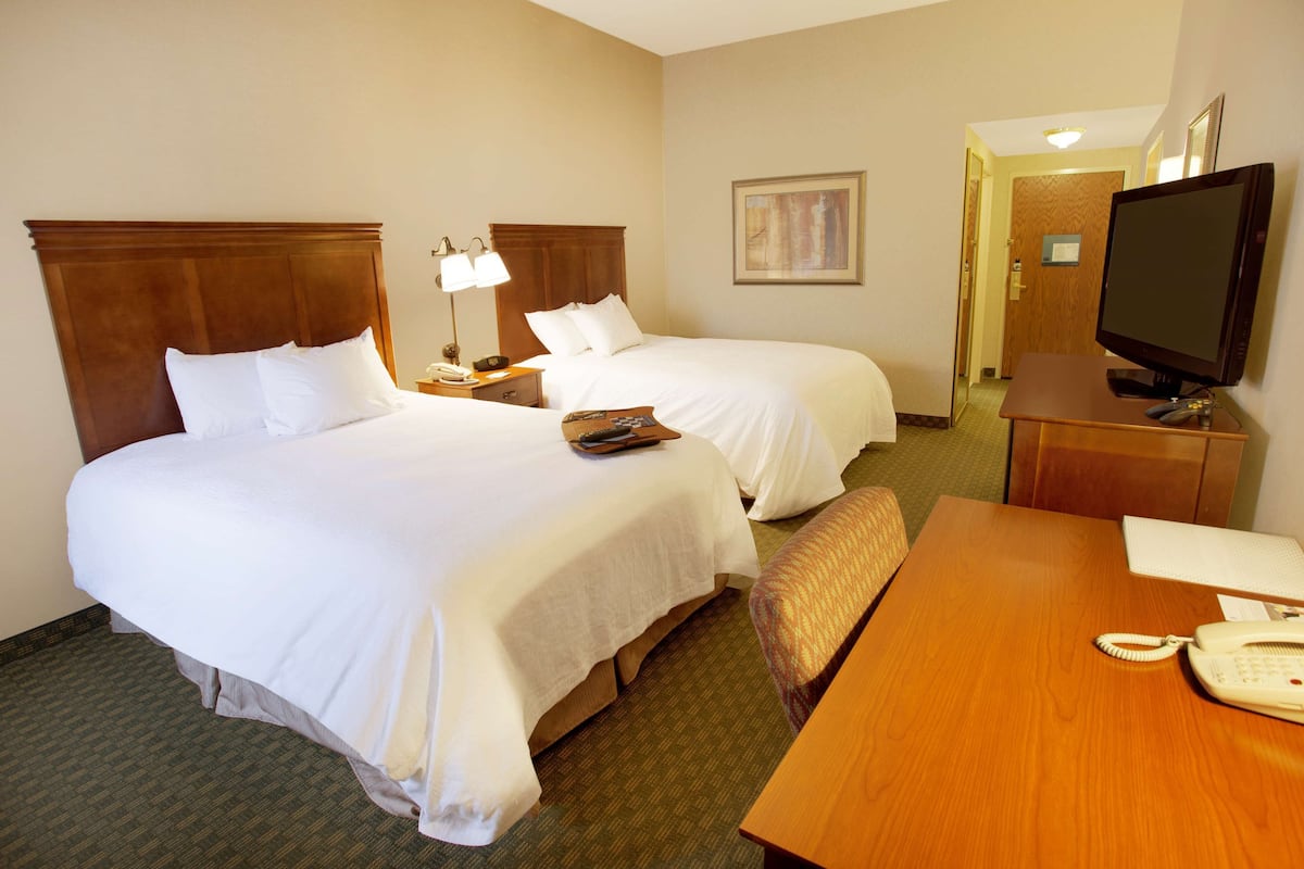 Quarto de hotel com duas camas, uma escrivaninha, uma televisão e um telefone.