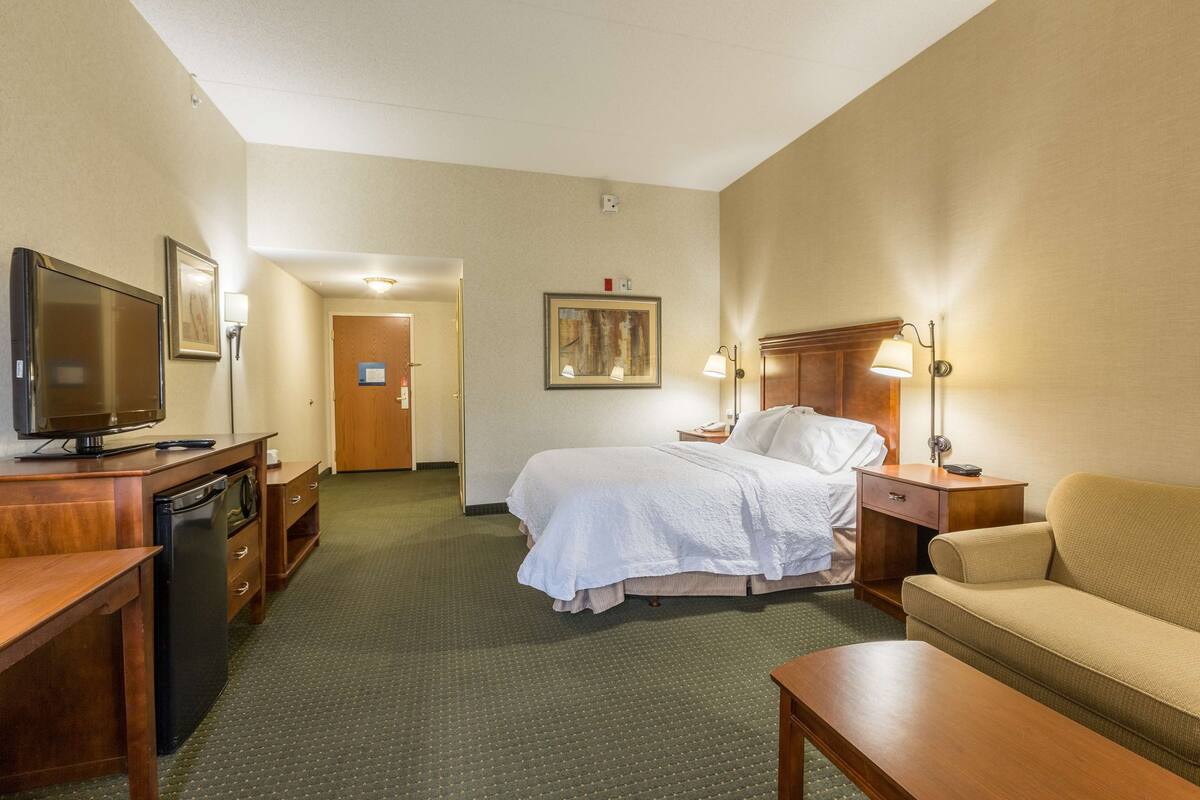 Quarto de hotel com cama, sofá, televisão, escrivaninha e abajur.