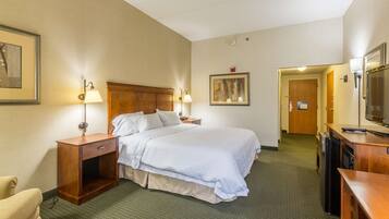 A hotel room with a bed, bedside tables, a desk with a computer, a TV, and a door leading to another room.