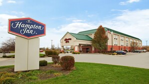 A Hampton Inn sign and a building with a green roof and beige walls. - Hampton Inn Sidney (Sidney)