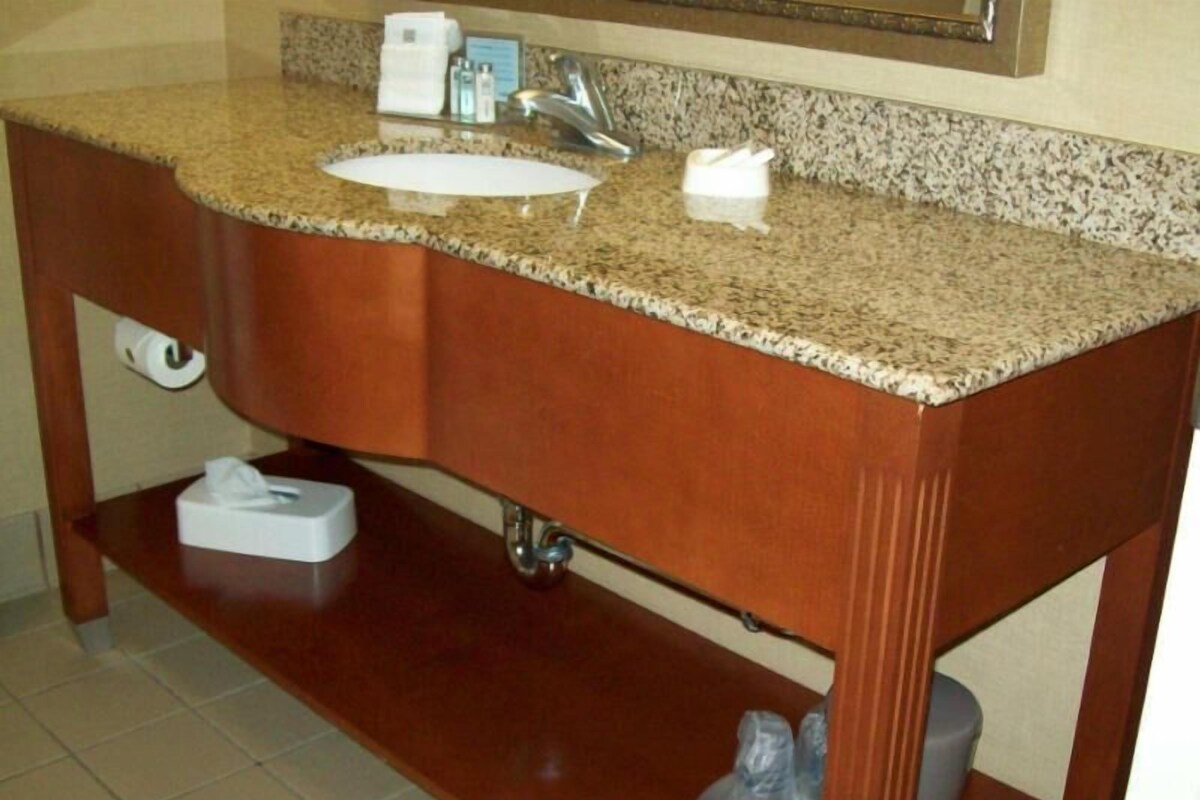 A bathroom with a granite countertop sink, a mirror, a towel dispenser, and a soap dispenser.