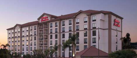A multi-story hotel with a prominent "Hampton Inn & Suites" sign, featuring a modern architectural design with a flat roof and uniform window patterns.